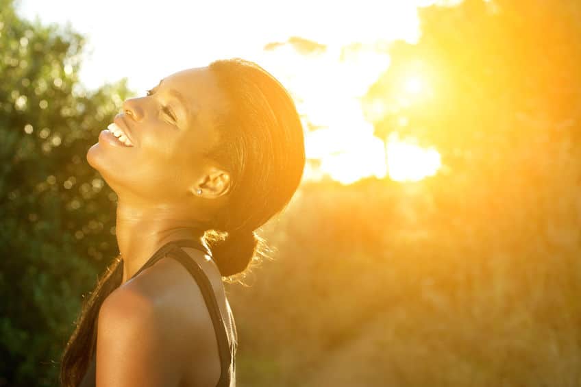 Photo of a smiling woman with the sun overexposed at the background