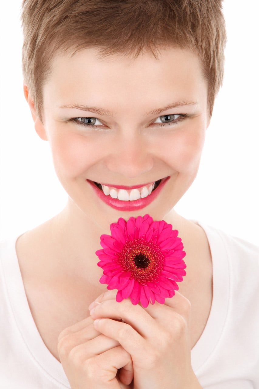 Young woman with short hair holding a bright pink flower covering her chin