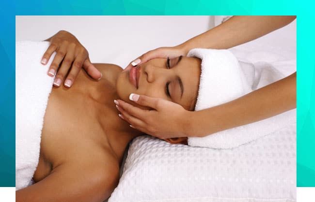 Female patient with towels in her hair and body, lying in table while having massage in her face