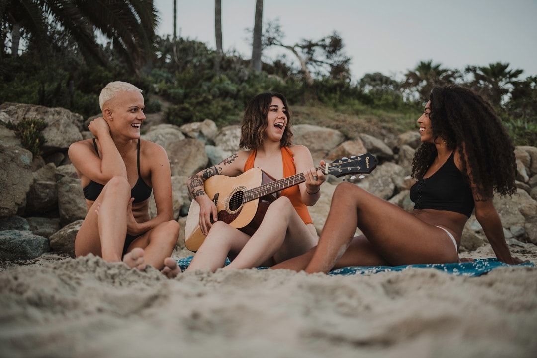 Group of diverse ladies in a beach singing with guitar accompaniment