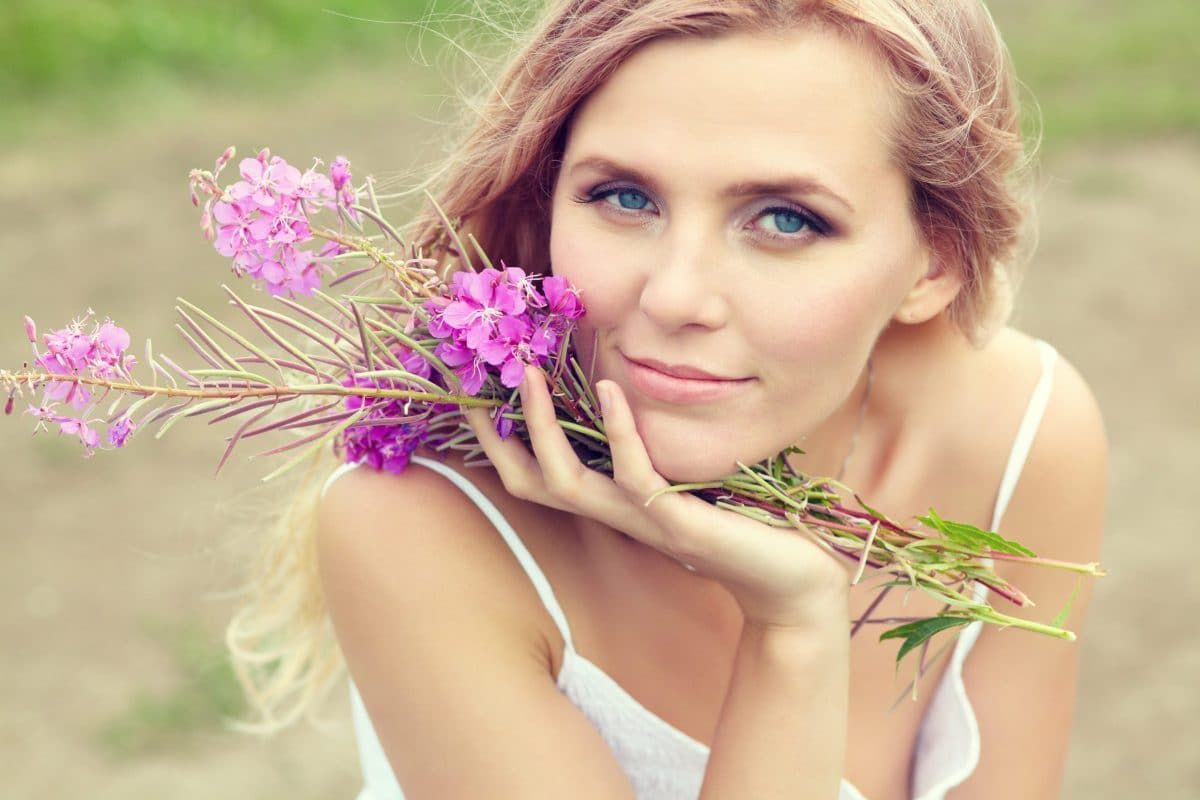 Young lady wearing white holding spring flowers and touching her face