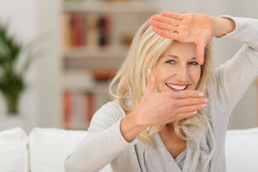 Happy mature woman in gray knits using her hands to frame her face in camera