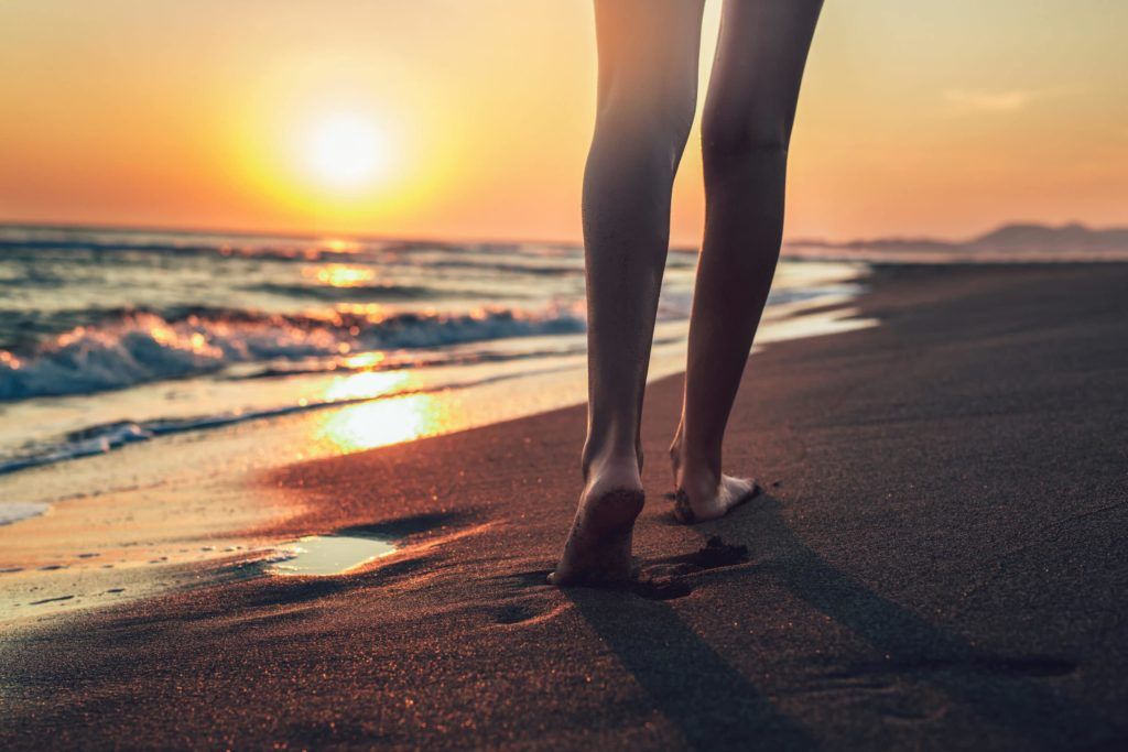 Walking in the beach shore during sunset, photo focuses the back of the legs