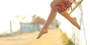 Photo of a woman sitting on a fence with legs hanging on air