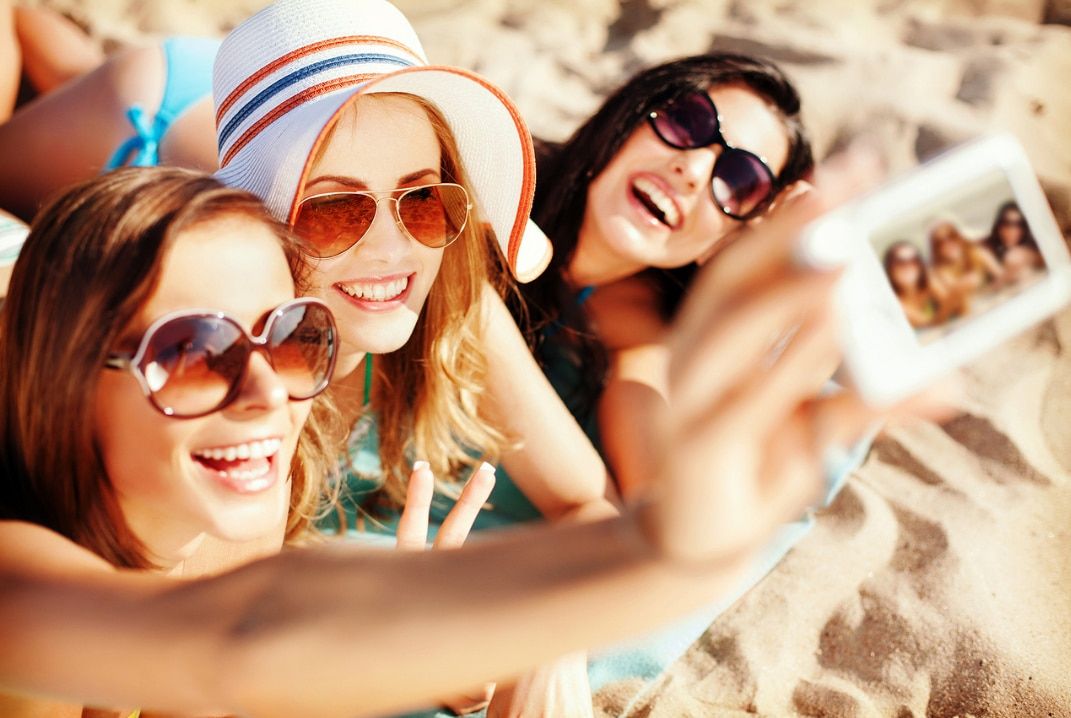 Three women sun bathing in the beach taking selfies together