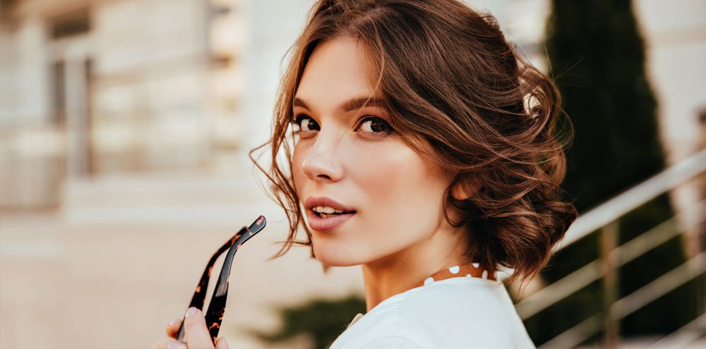 Sensual young woman in white blouse looking over shoulder. Positive elegant girl with short hair posing on the street.